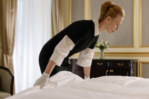 Camarera de hotel haciendo la cama en una habitación elegante, usando guantes y uniforme.