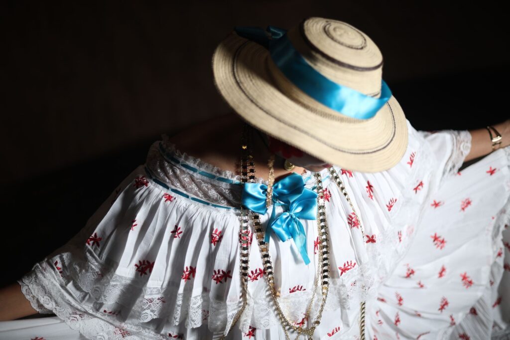 Un primer plano de un vestido tradicional de pollera adornado con un sombrero de paja y una vibrante cinta azul, que muestra la elegancia cultural.